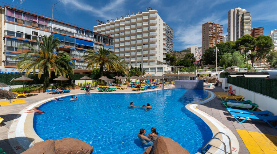 Swimming pool at Hotel Poniente with the hotel in the background with palm trees.