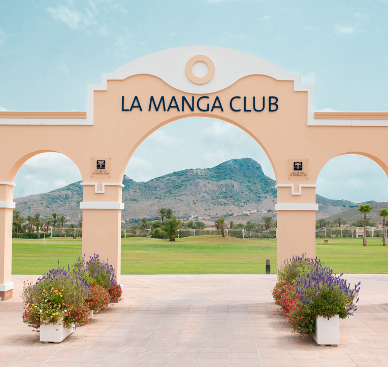 An arch at the La Manga Golf Resort with the words "La Manga Club" at the top and the course and moutains in the background.